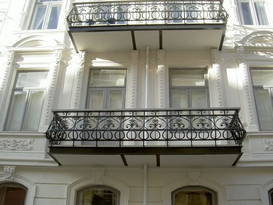 Balkong med svart gelender på hvit husfasade